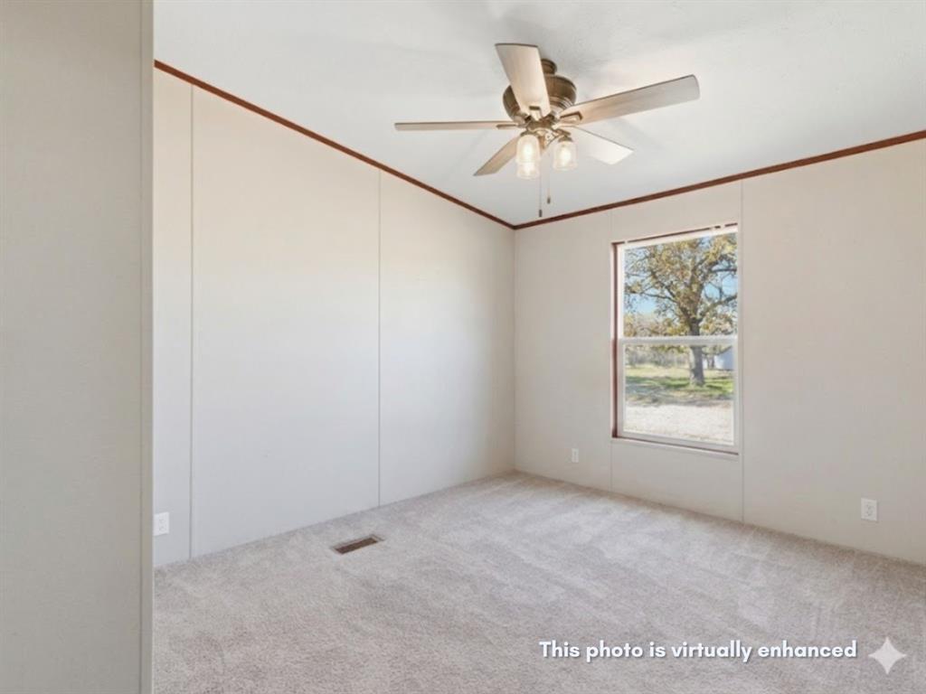2722 Denver Road Sunset, TX 76270 - Photo 9 of 19 Room featuring light gray wall panels with brown trim, a window with exterior scenery, a ceiling fan with integrated lighting, and light gray carpet flooring
