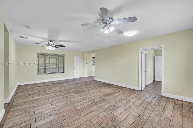 a view of an empty room with wooden floor and a ceiling fan