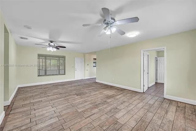 a view of an empty room with wooden floor and a ceiling fan