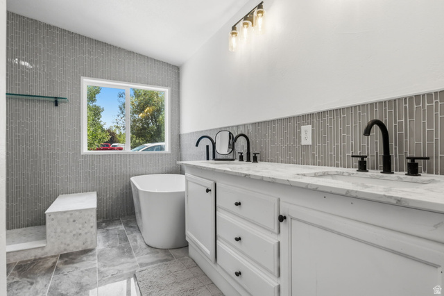 4270 River Road Oakley, UT 84055 - Photo 11 of 46 Contemporary bathroom featuring a freestanding tub, a dual vanity with marble-finish countertops, black hardware and fixtures, and a glass tile accent wall