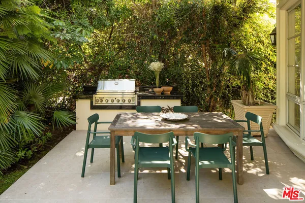 a patio with table and chairs with potted plants and large trees