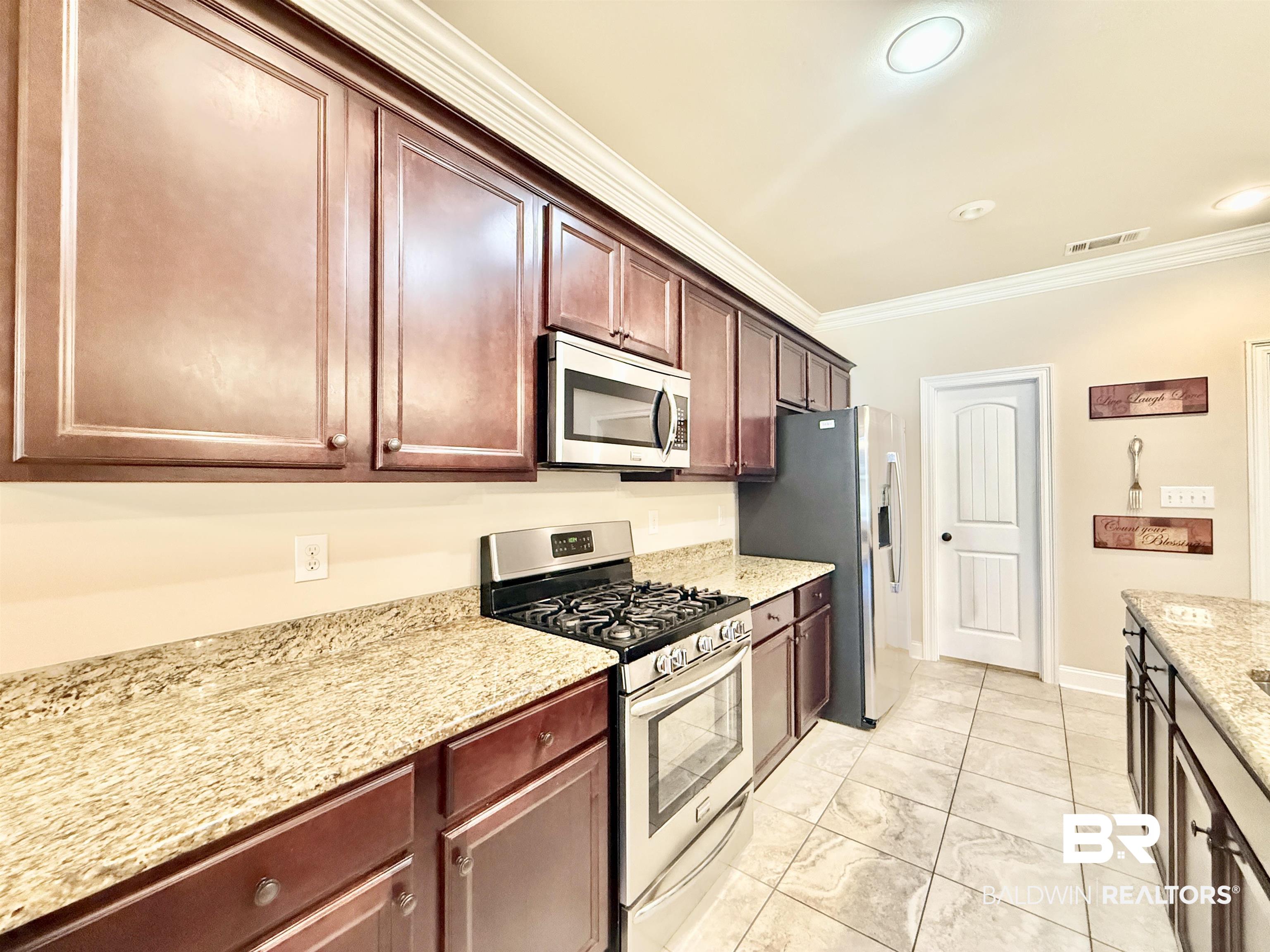 7011 Rocky Rd Loop Gulf Shores, AL 36542 - Photo 2 of 66 Kitchen featuring stainless steel appliances, crown molding, light stone counters, and dark brown cabinetry