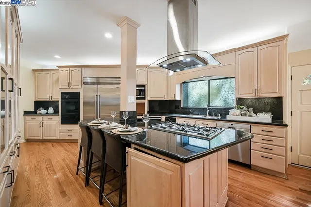 a kitchen with stainless steel appliances granite countertop a stove a sink dishwasher a refrigerator and white cabinets with wooden floor