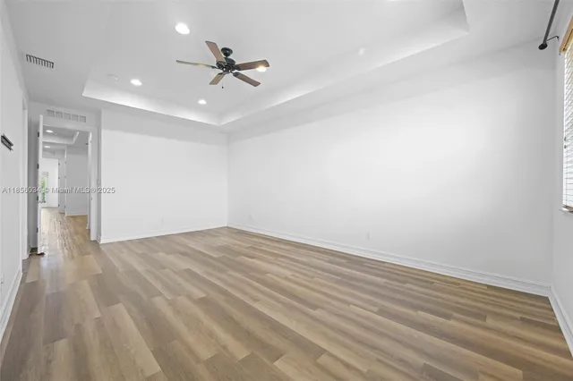 a view of an empty room with wooden floor and a ceiling fan
