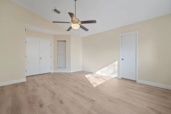 a view of an empty room with wooden floor and a ceiling fan