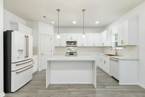 a kitchen with stainless steel appliances kitchen island granite countertop a refrigerator a stove and white cabinets with wooden floors