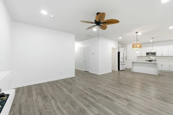 a view of an empty room with wooden floor and a ceiling fan