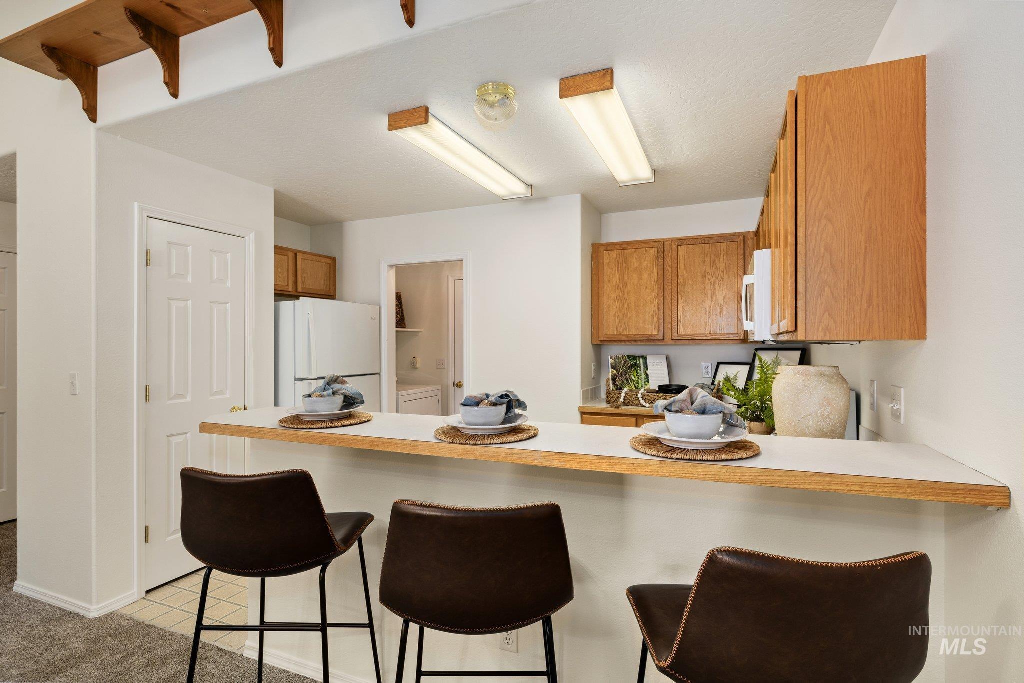 2900 South Ladera Place Boise, ID 83705 - Photo 10 of 31 Kitchen featuring a kitchen bar, light countertops, white appliances, brown cabinets, and a peninsula