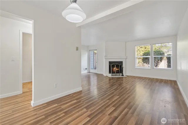 an empty room with wooden floor fireplace and windows