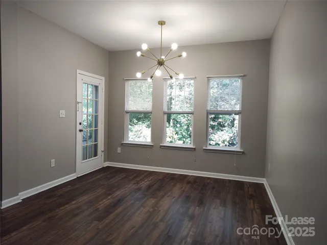 an empty room with wooden floor chandelier and windows