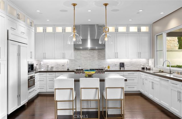 a kitchen with stainless steel appliances granite countertop a stove a sink a refrigerator and white cabinets with wooden floor