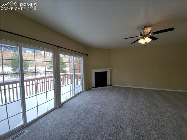 an empty room with chandelier fan and windows