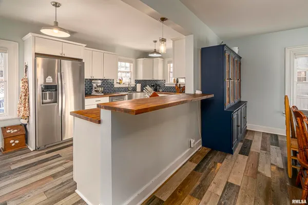 a kitchen with stainless steel appliances granite countertop a refrigerator a sink dishwasher a stove and a dining table with wooden floor
