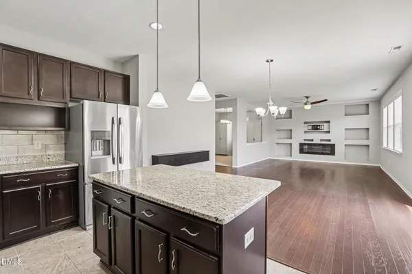 a kitchen with granite countertop a stove a kitchen island a sink dishwasher a refrigerator and wooden floor