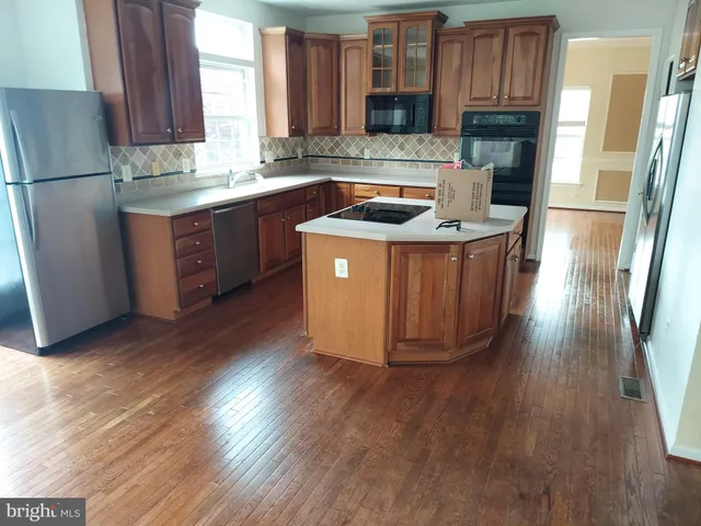 a kitchen with stainless steel appliances granite countertop a refrigerator a sink dishwasher a stove a refrigerator and dishwasher with wooden floor