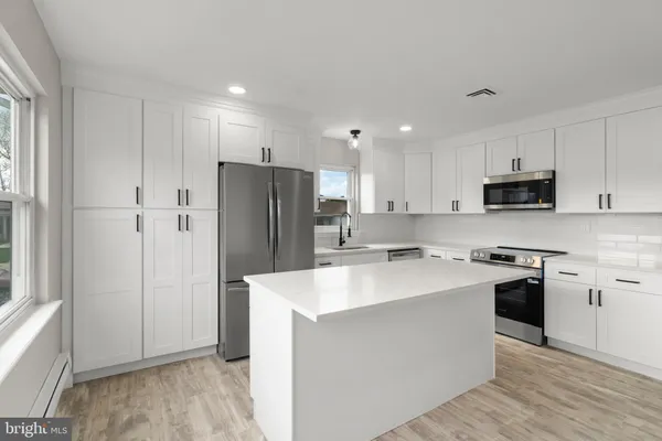 a kitchen with stainless steel appliances granite countertop a refrigerator stove a sink and white cabinets with wooden floor