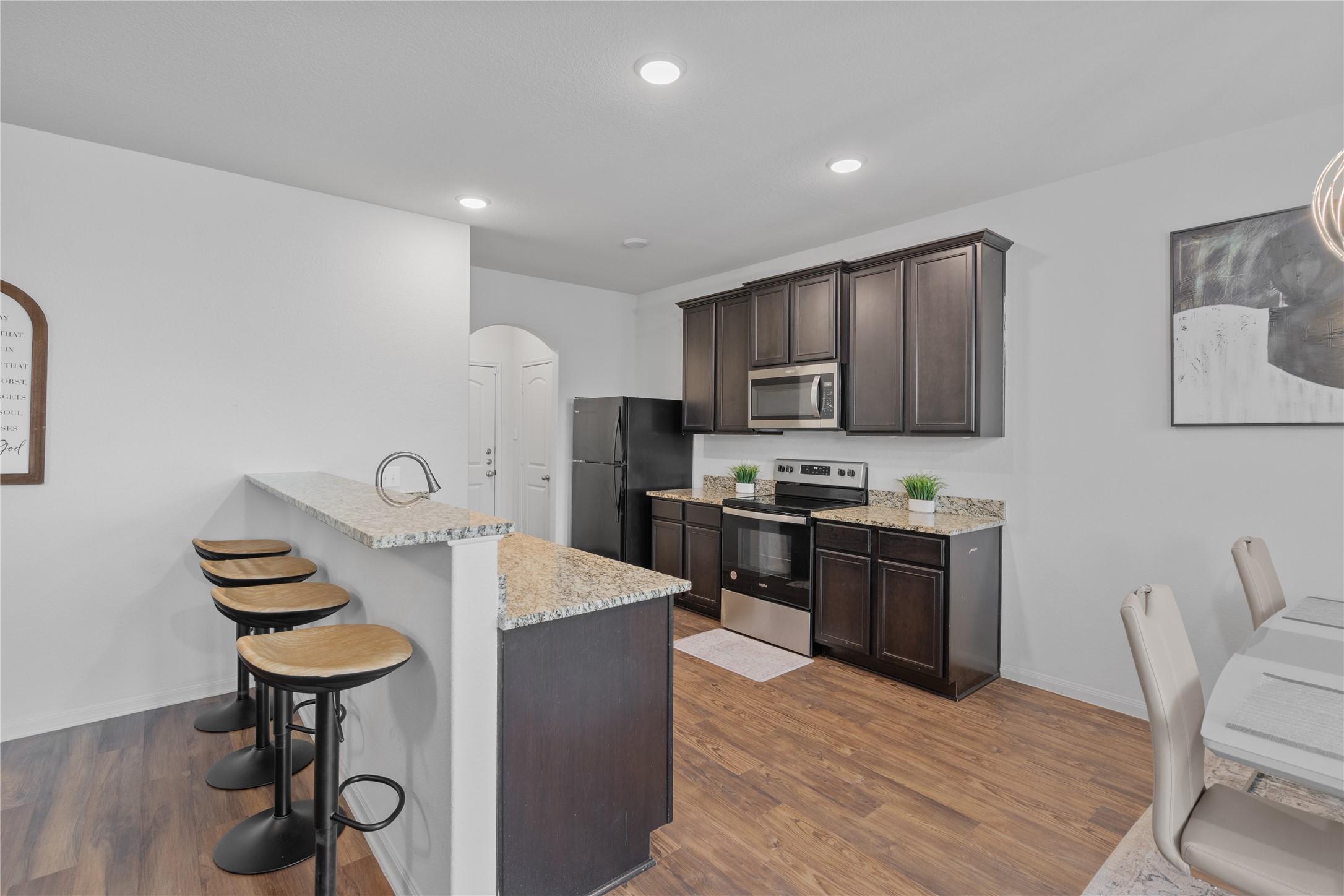 20205 Grover Cleveland Way Manor, TX 78653 - Photo 9 of 26 a kitchen with stainless steel appliances kitchen island granite countertop a stove a sink dishwasher a dining table and chairs with wooden floor