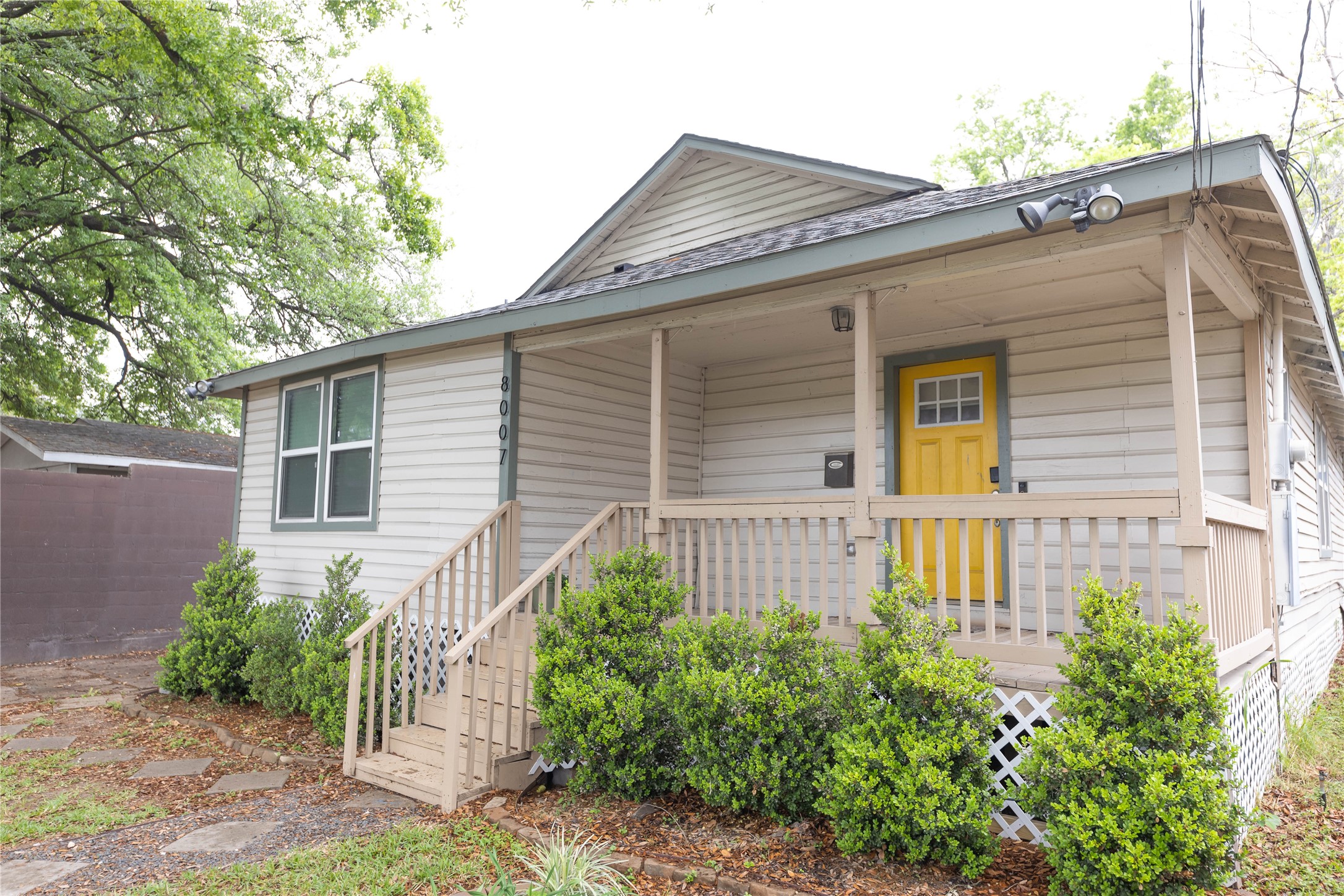 8007 Capitol Street Houston, TX 77012 - Photo 4 of 25 Charming single-story home with a welcoming front porch. The exterior is accented by lush greenery and mature trees, creating a cozy and inviting atmosphere.