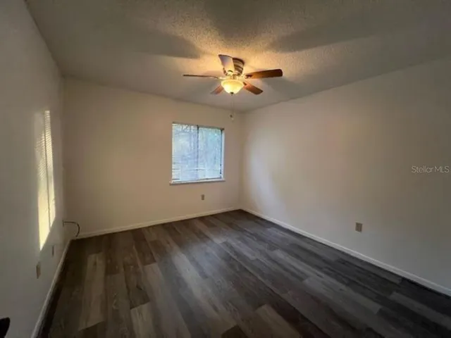 an empty room with wooden floor fan and windows