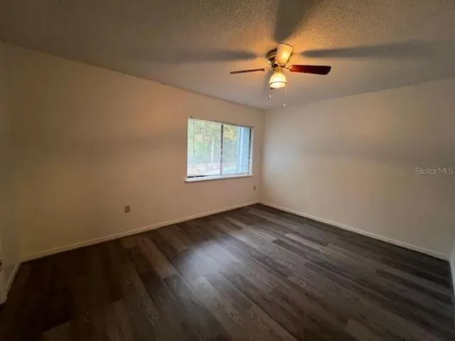 an empty room with wooden floor fan and windows
