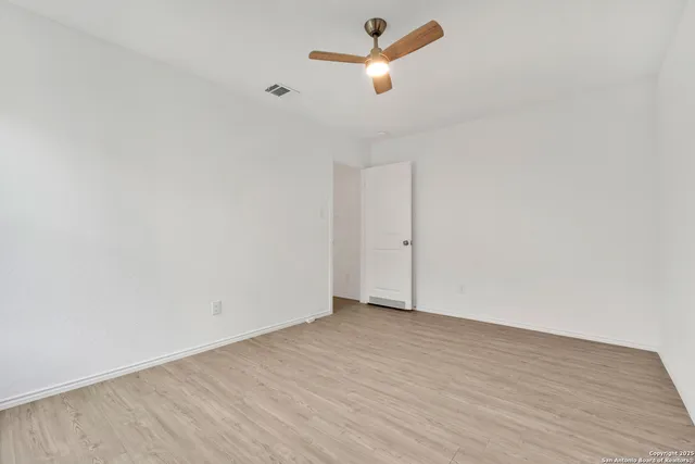 an empty room with wooden floor ceiling fan and window