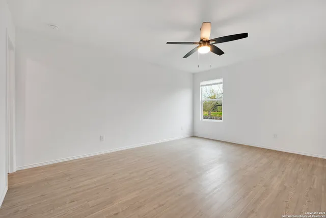 an empty room with wooden floor ceiling fan and windows