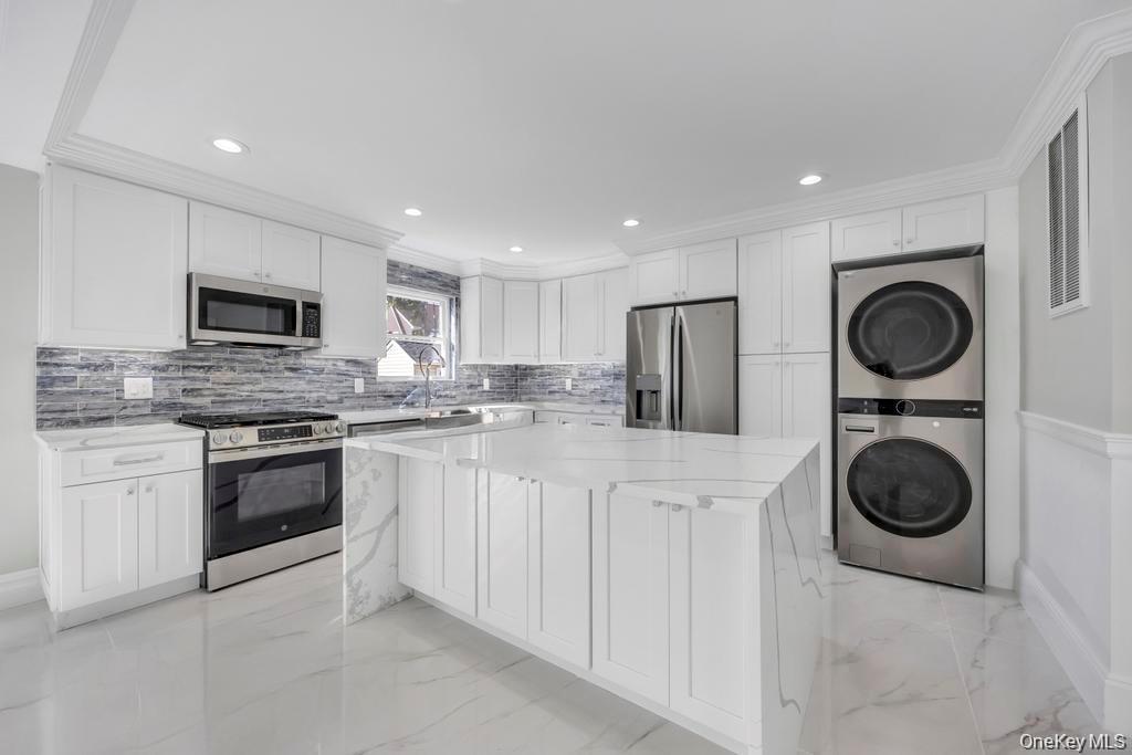 Kitchen featuring stainless steel appliances, white cabinets, light stone countertops, stacked washer / drying machine, and a center island