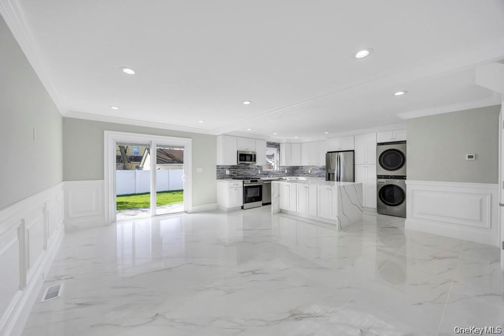 41 Perry Street Hempstead, NY 11550 - Photo 2 of 36 Kitchen featuring a wainscoted wall, a decorative wall, white cabinetry, ornamental molding, and stacked washing machine and dryer