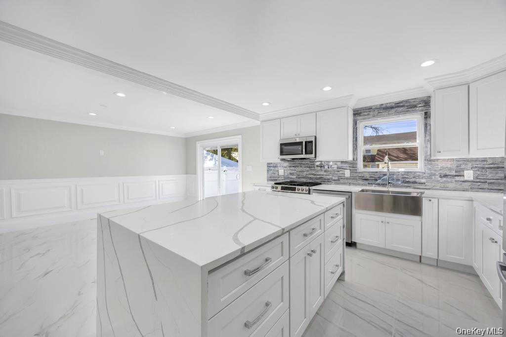 41 Perry Street Hempstead, NY 11550 - Photo 7 of 36 Kitchen with light marble finish flooring, a wainscoted wall, a center island, white cabinetry, and a decorative wall