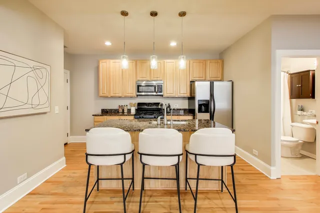 a kitchen with stainless steel appliances a refrigerator a stove a dining table and chairs with wooden floor