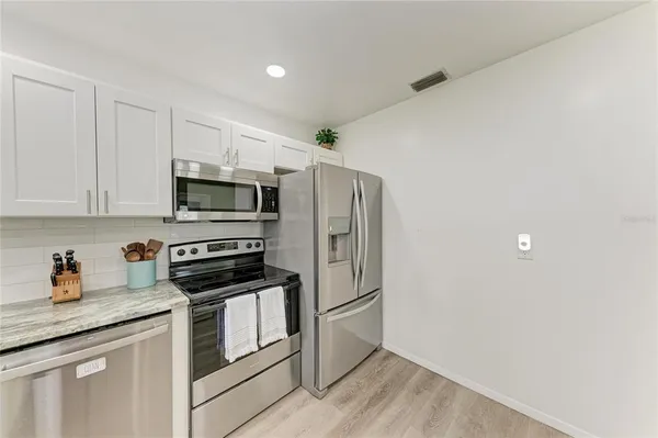 a kitchen with stainless steel appliances granite countertop a refrigerator a stove top oven a sink dishwasher and white cabinets with wooden floor