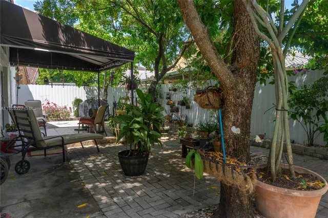 a view of a backyard with table and chairs potted plants and a large tree