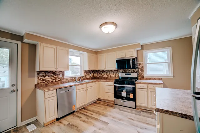 a kitchen with stainless steel appliances granite countertop a stove top oven a sink dishwasher and white cabinets with wooden floor