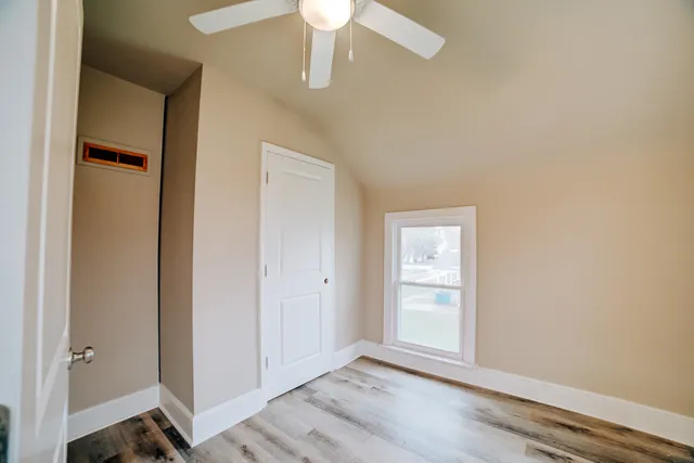 an empty room with wooden floor closet and windows
