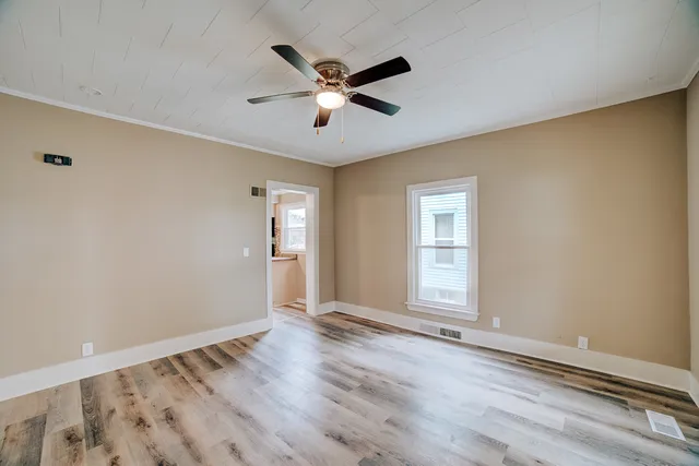 an empty room with wooden floor fan and windows