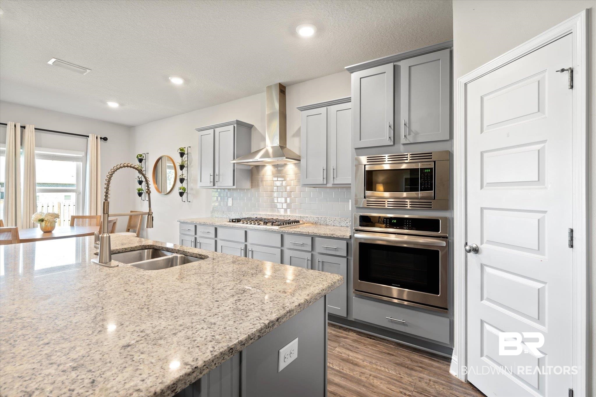 12899 Sanderling Loop Daphne, AL 36527 - Photo 11 of 28 Kitchen with wall chimney range hood, appliances with stainless steel finishes, light stone countertops, dark hardwood / wood-style floors, and sink