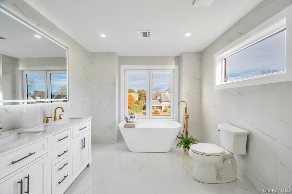 126 Rim Lane Hicksville, NY 11801 - Photo 13 of 28 Bathroom with stone wall, double vanity, a freestanding tub, light marble finish floors, and plenty of natural light