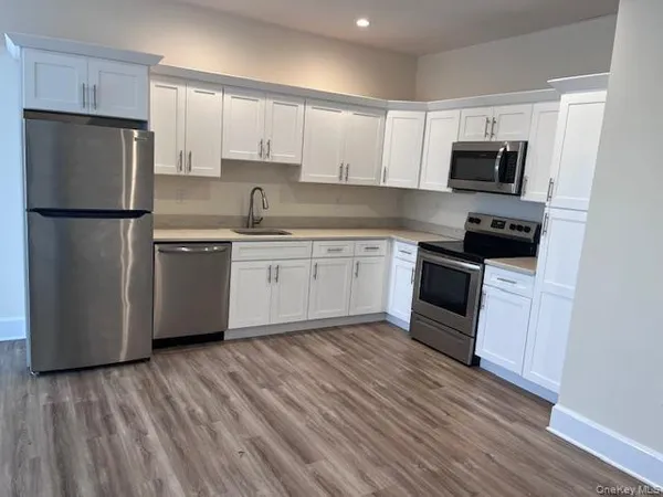 a kitchen with stainless steel appliances granite countertop a refrigerator a stove top oven a sink and dishwasher with wooden floor