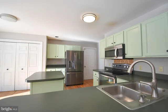 a kitchen with stainless steel appliances granite countertop a sink a stove a refrigerator cabinets and a dining table