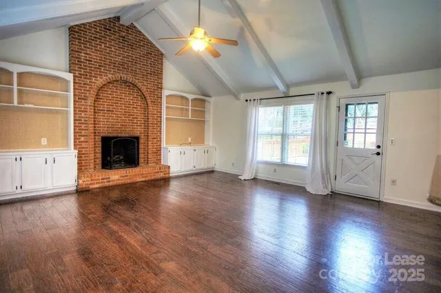 an empty room with wooden floor fireplace and windows