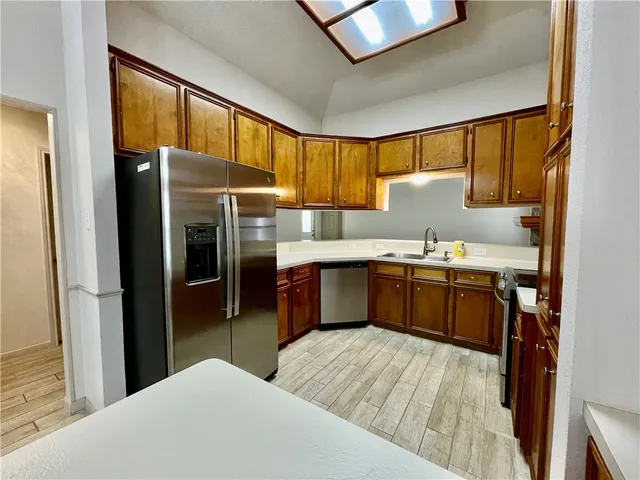 a kitchen with stainless steel appliances kitchen island granite countertop a refrigerator a sink dishwasher and a stove with wooden cabinets