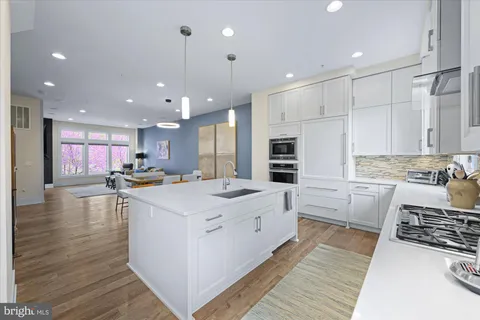 a large white kitchen with kitchen island a stove a sink a refrigerator and white cabinets with wooden floor