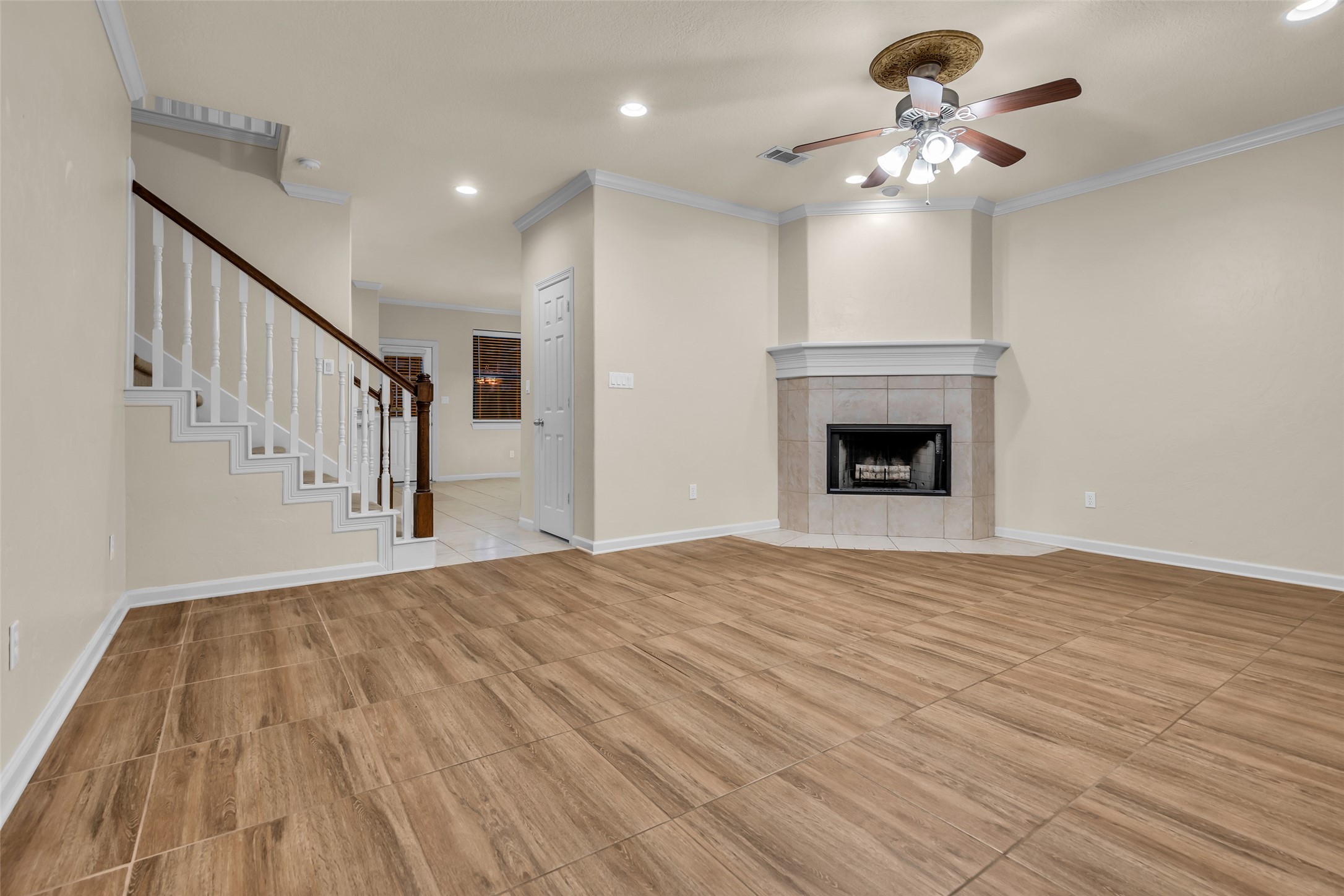 1898 Longmire Road, Unit 5 Conroe, TX 77304 - Photo 11 of 48 This spacious living area features wood-like tile flooring, a cozy fireplace, and a ceiling fan. The room is well-lit with recessed lighting and natural light from a nearby window. A staircase with a white railing leads to the upper level, adding an elegant touch.