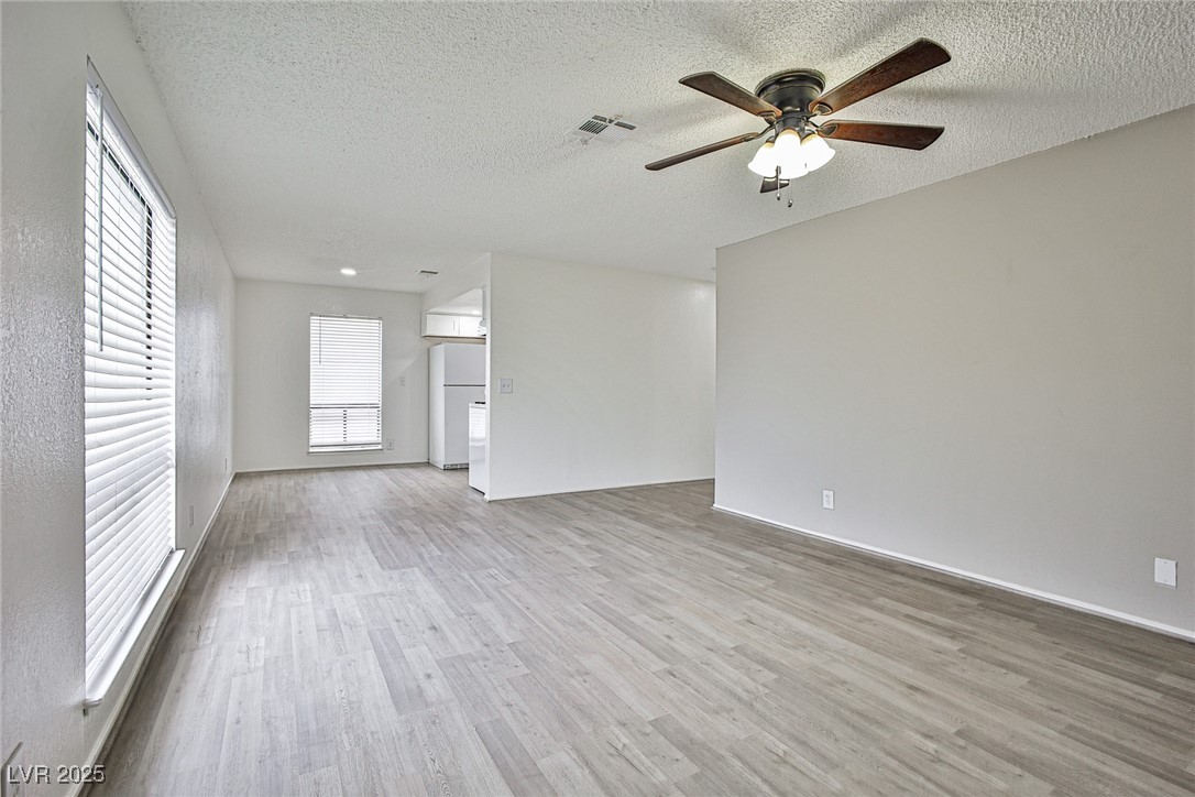 Unfurnished living room with ceiling fan, a textured ceiling, and wood finished floors