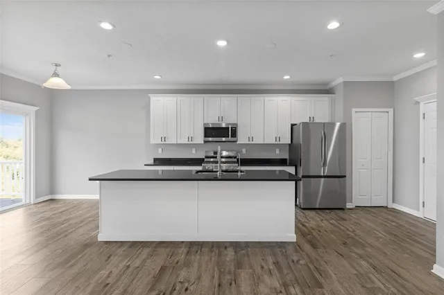 a kitchen with stainless steel appliances granite countertop a refrigerator a sink a stove a microwave and white cabinets with wooden floor