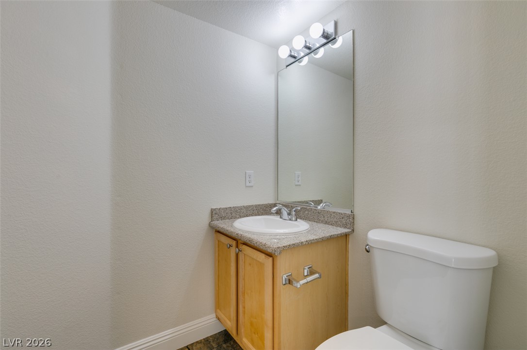 200 Luninborg Street Henderson, NV 89074 - Photo 13 of 40 A compact half bath features a light wood vanity, granite-style countertop, and a vanity mirror with sleek overhead lighting.