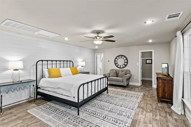 a bedroom with a bed a dresser next to a large window with the outer view and chair