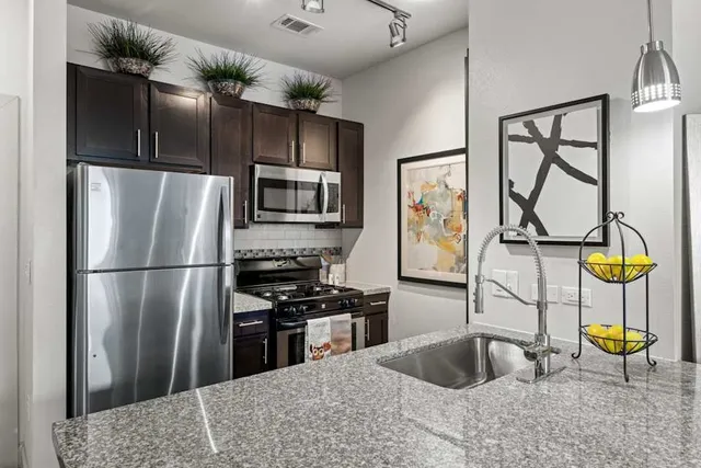 a kitchen with stainless steel appliances granite countertop a refrigerator a stove and a sink with wooden floor