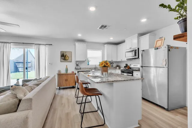 a kitchen with stainless steel appliances granite countertop a refrigerator a sink a stove a dining table and chairs