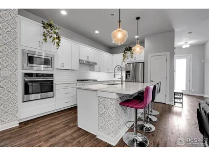 a open kitchen with stainless steel appliances kitchen island granite countertop a sink dishwasher a microwave oven a stove with white cabinets and wooden floor